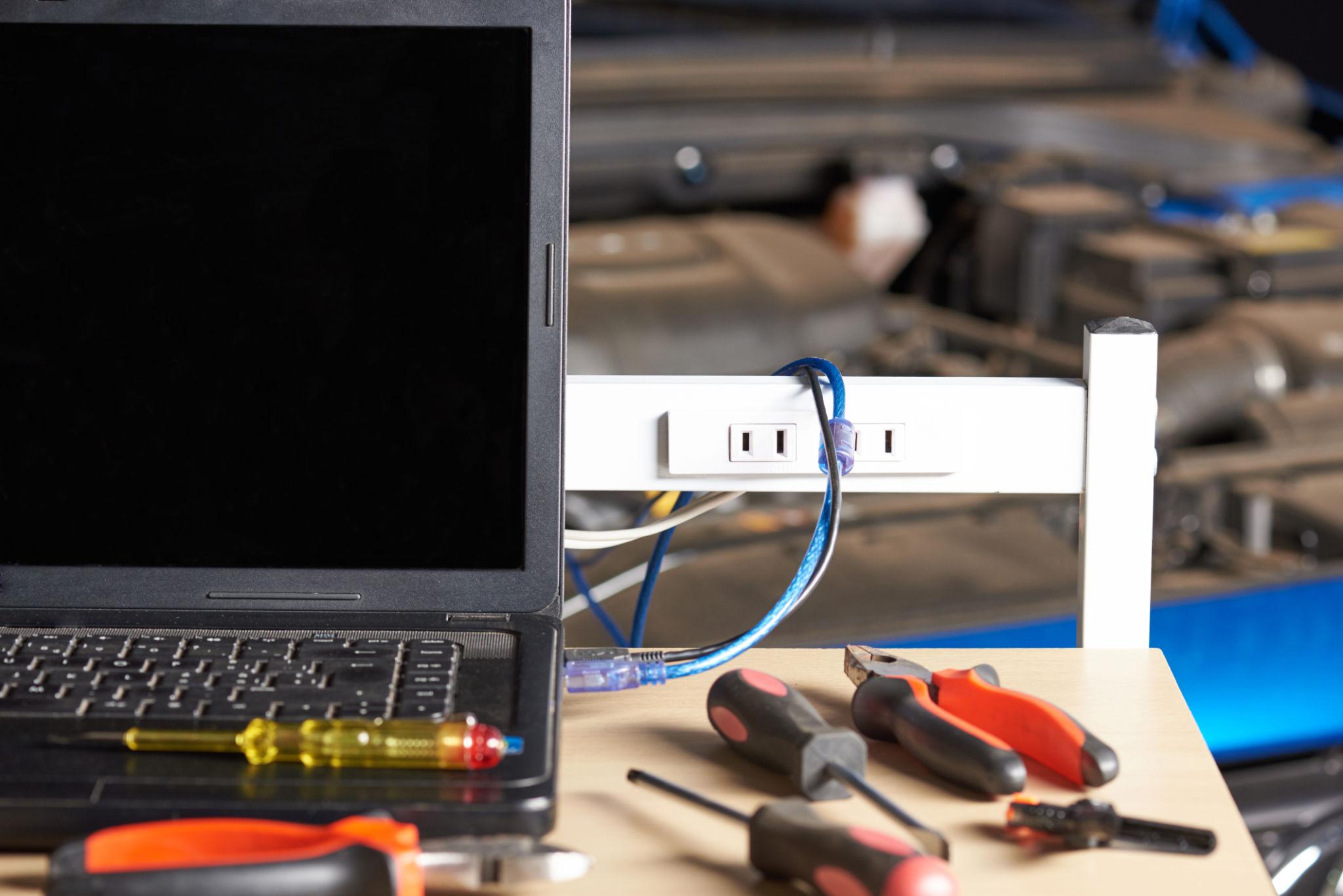 Automotive diagnostic tools set — OBD-II scanner with live data display, digital multimeter, compression tester, and digital calipers on a workshop bench
